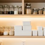 Organisation des placards de cuisine : gagner du temps chaque jour Placards de cuisine lumineux et bien organisés, avec des bocaux transparents et des boîtes hermétiques dans une ambiance chaleureuse.