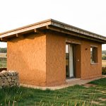 Petite maison contemporaine en terre crue aux murs ocre, installée dans un paysage rural français sous une lumière douce.